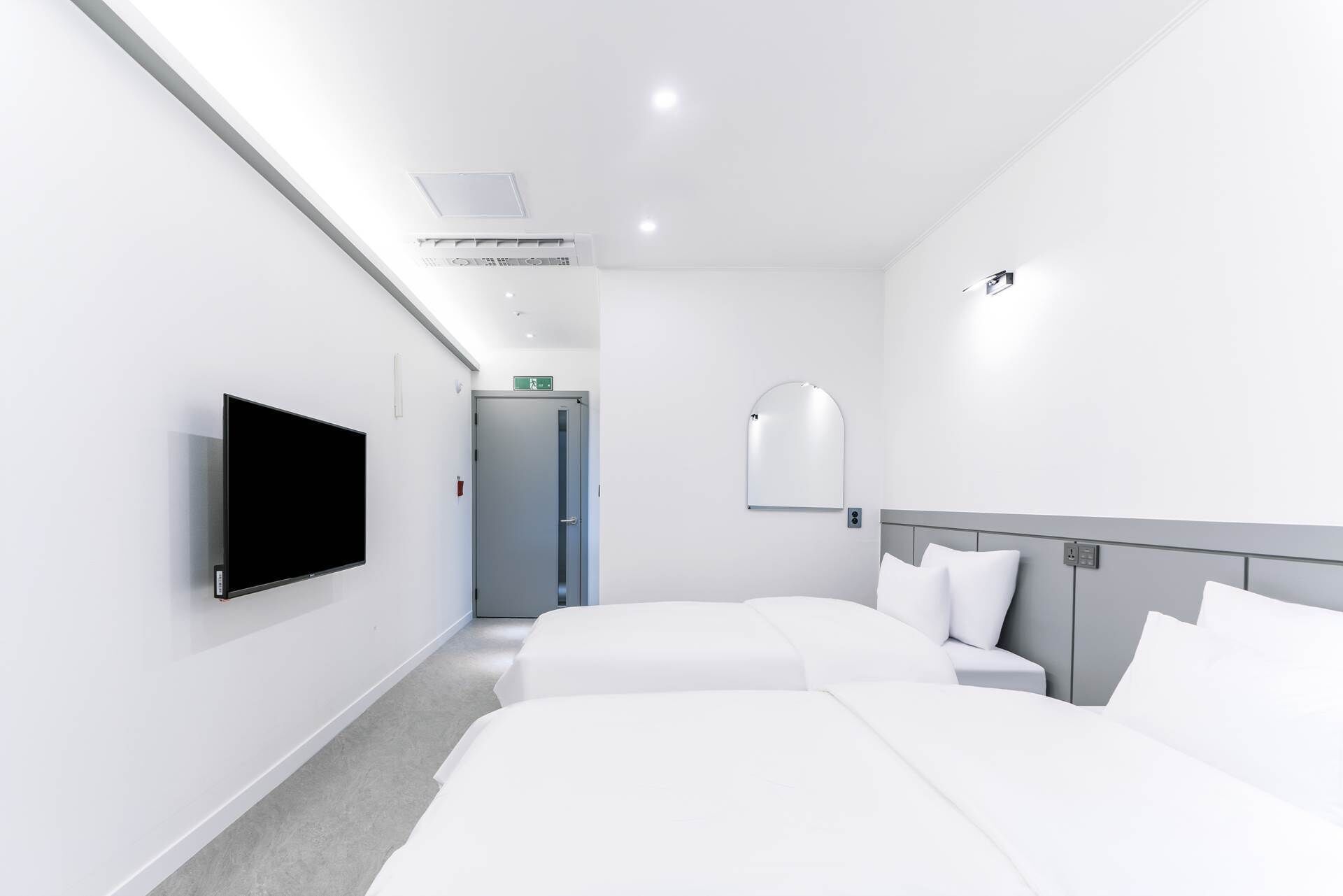 Habitación de hotel con dos camas, un televisor de pantalla plana, un espejo y una puerta que da a un pasillo.