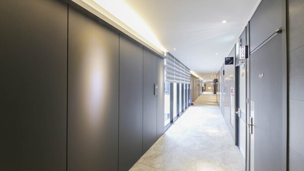 A modern hotel corridor with a long, narrow layout, featuring a series of doors on one side and a glass wall on the other.