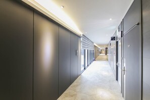 Un pasillo de hotel moderno con una distribución larga y estrecha, con una serie de puertas en un lado y un muro de vidrio en el otro.