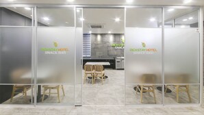 A modern hotel snack bar with glass partitions, wooden chairs, and a counter with a menu display.