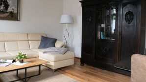 A living room with a beige sofa, a dark wooden cabinet, a white lamp, and a wooden coffee table. - Holiday apartment Käte (ferienwohnungen1886) (Borsdorf)
