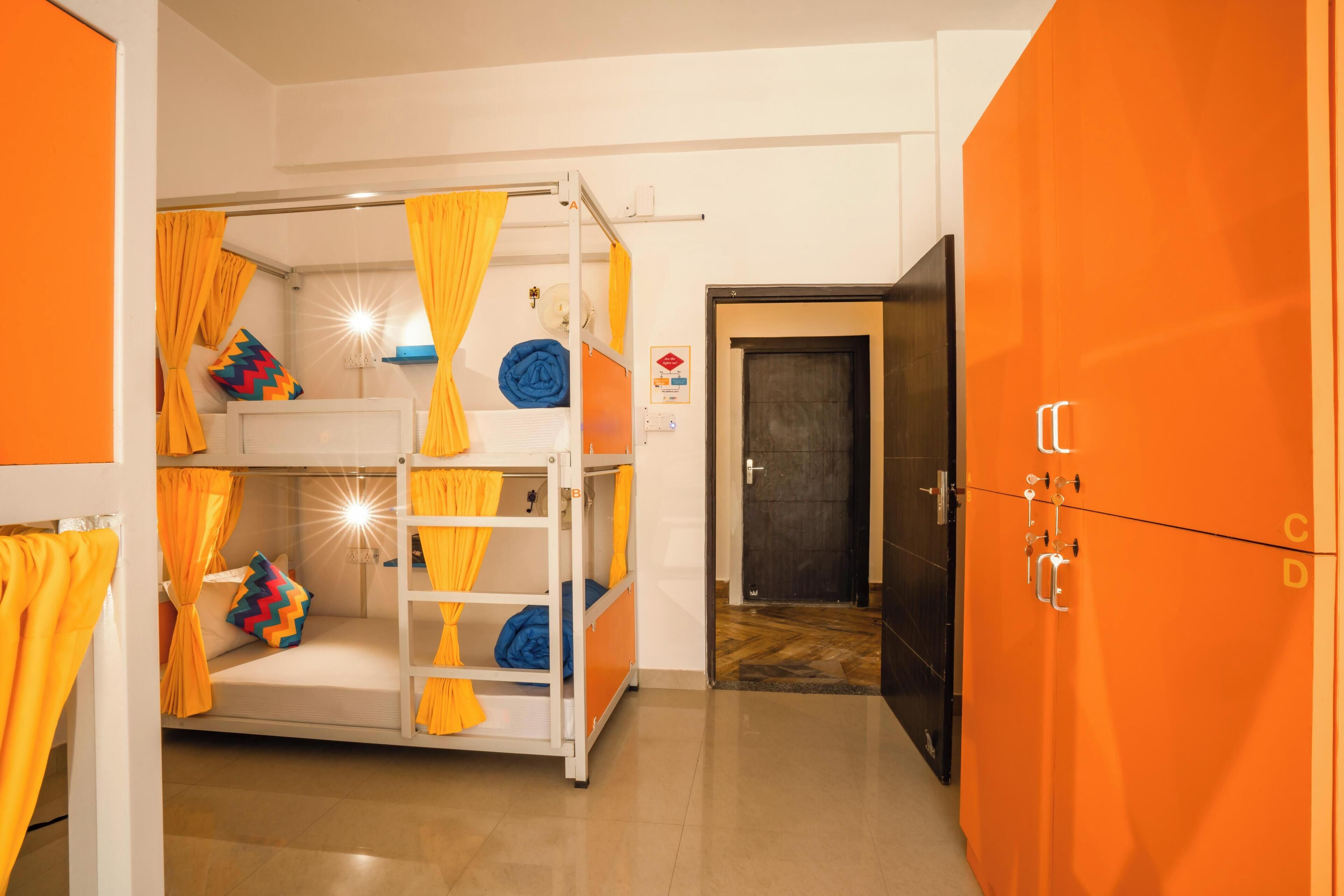 Una cama litera con cortinas amarillas, una pared blanca con un interruptor de luz y un armario naranja con cerradura.