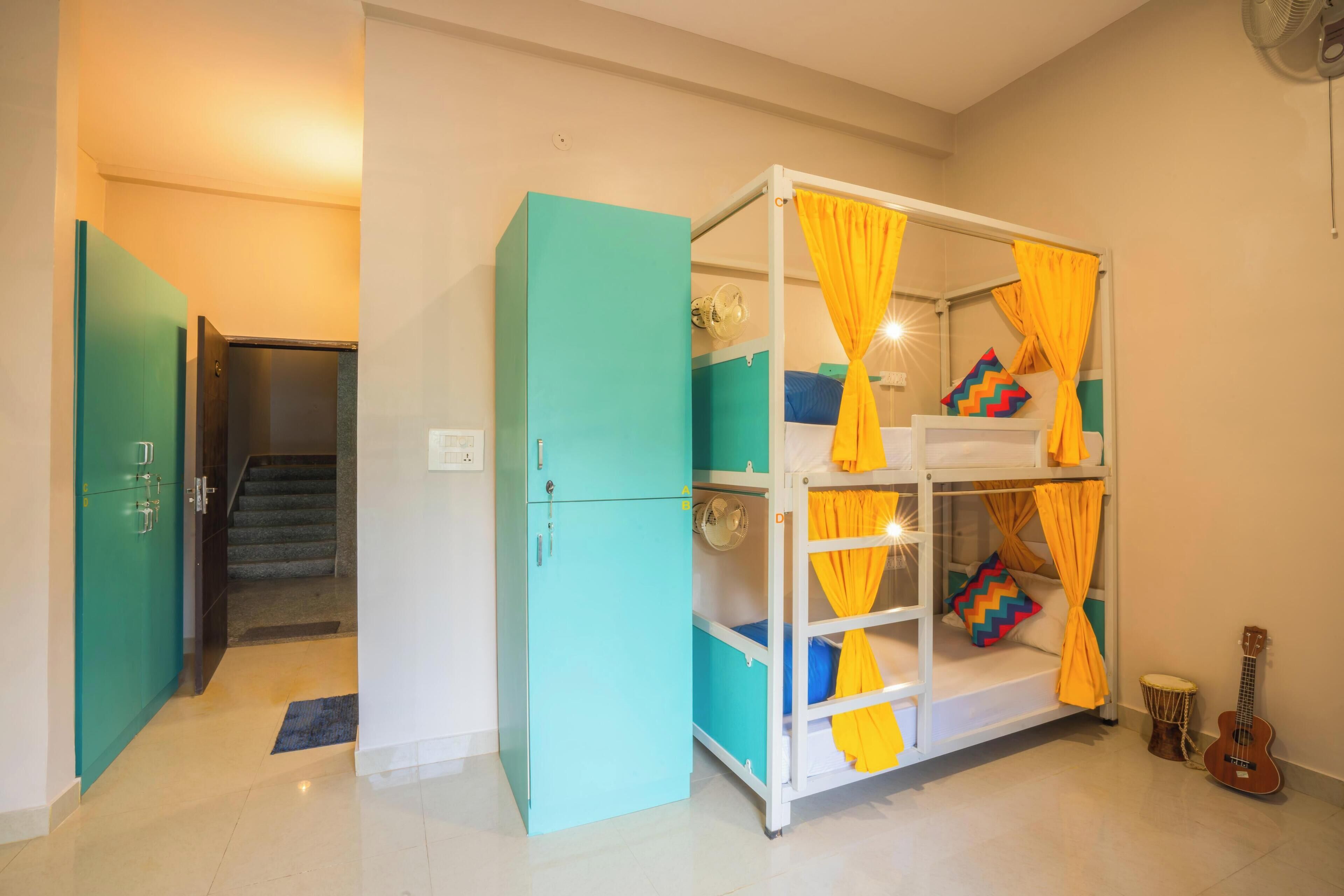 A room with a bunk bed, a teal wardrobe, a guitar, and a staircase.