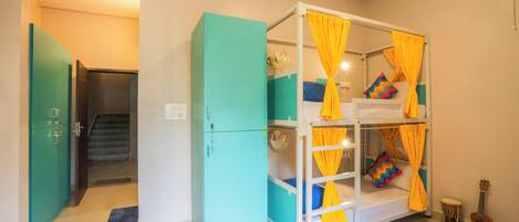 A room with a bunk bed, a teal wardrobe, a guitar, and a staircase.