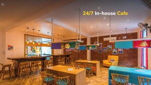A 24/7 in-house cafe with wooden furniture, hanging lights, and a brick wall. - goSTOPS Rishikesh, Lakshman Jhula (Yamkeshwar)
