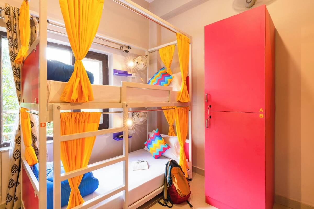 Una cama litera con cortinas amarillas, un armario rojo y una mochila en el suelo.