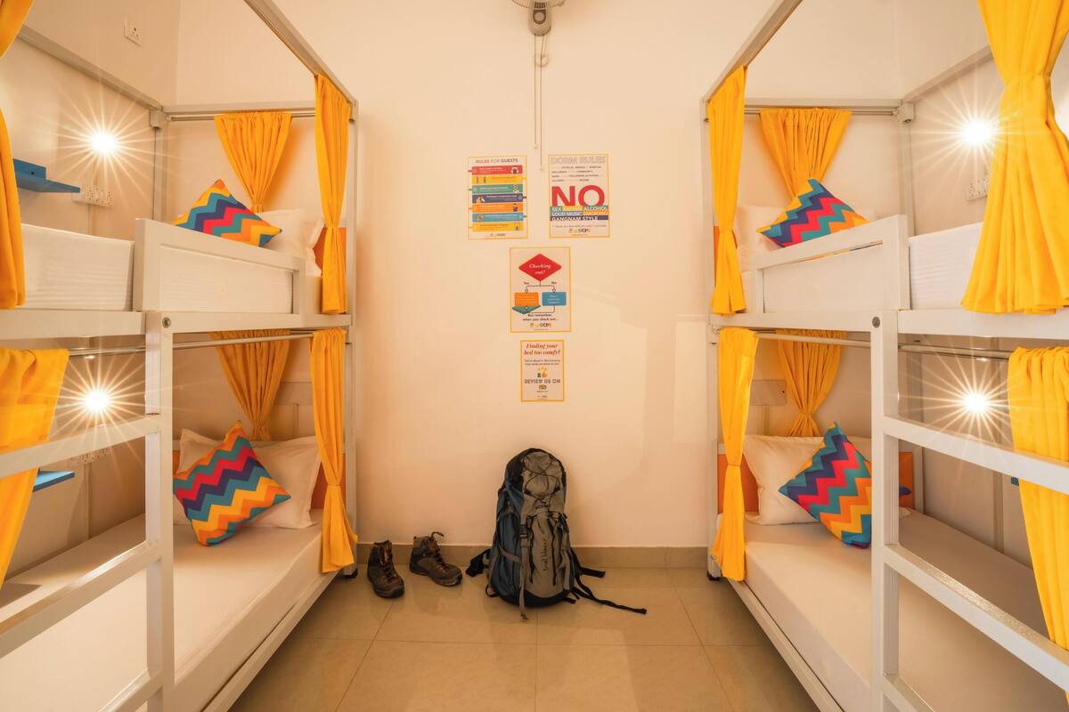Un dormitorio con literas, cortinas amarillas y una mochila en el suelo.