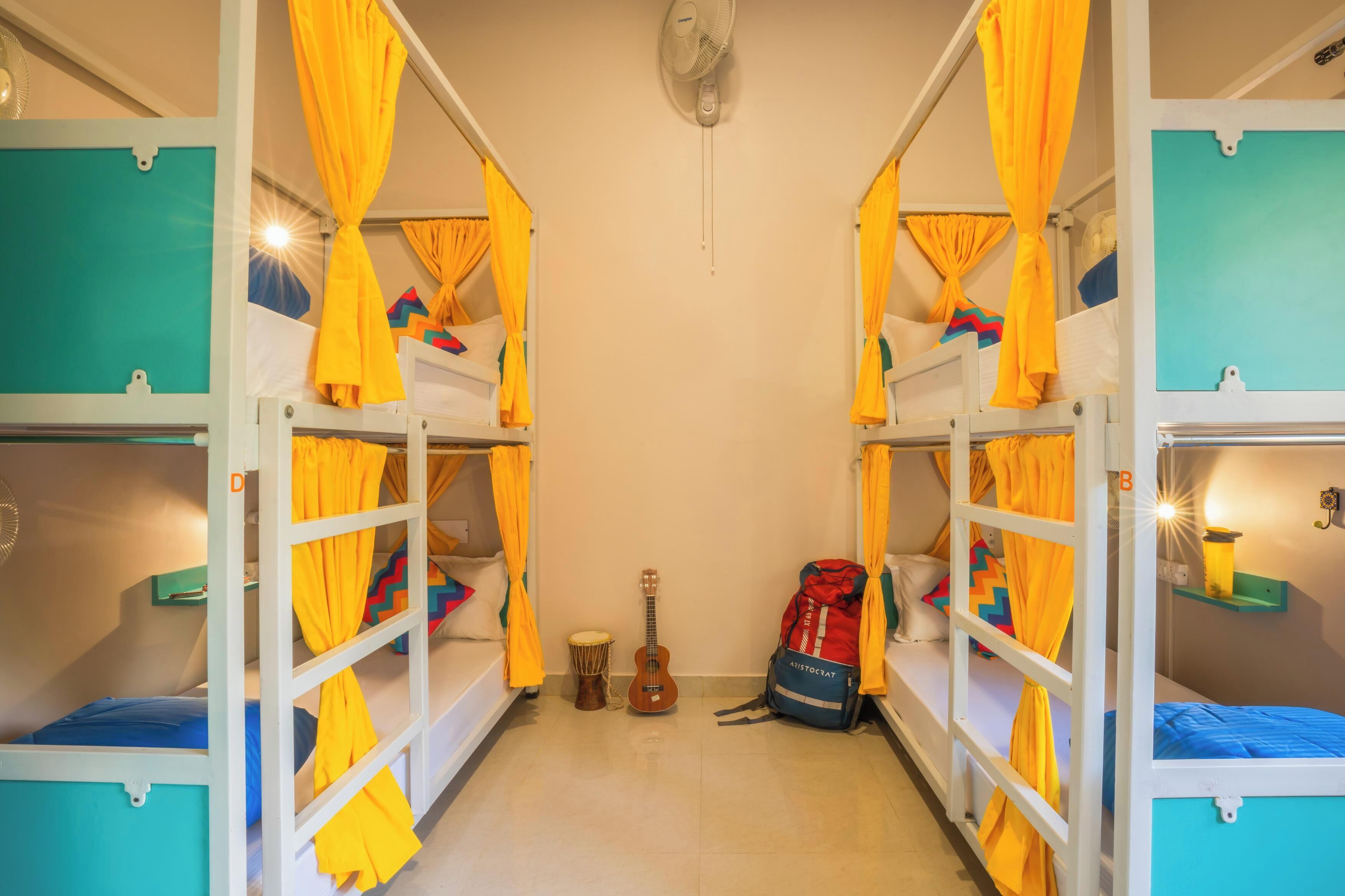 A dormitory room with bunk beds, a guitar, a drum, and a backpack.