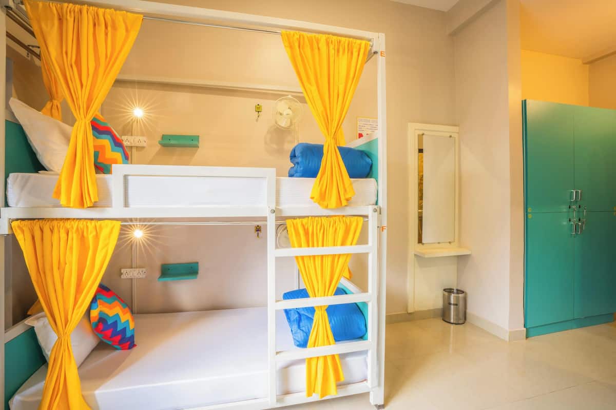 Habitación con literas, cortinas amarillas, un mueble de color aguamarina y un ventilador blanco.