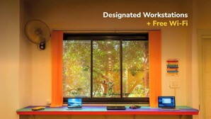 A designated workstation with a laptop, a fan, and a window with curtains. - goSTOPS Rishikesh, Lakshman Jhula (Yamkeshwar)