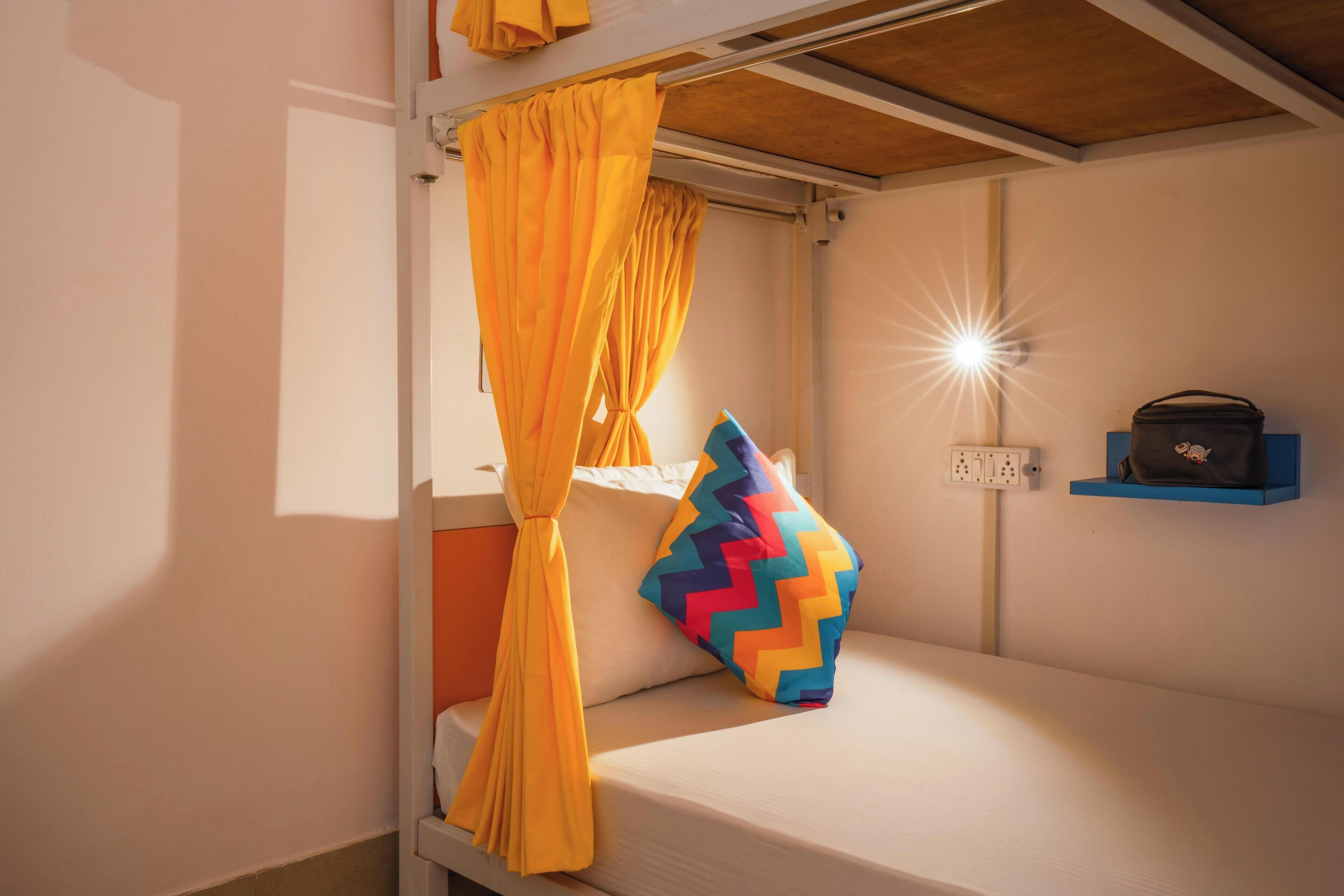 A bunk bed with yellow curtains, a colorful zigzag pillow, and a wall-mounted light fixture.