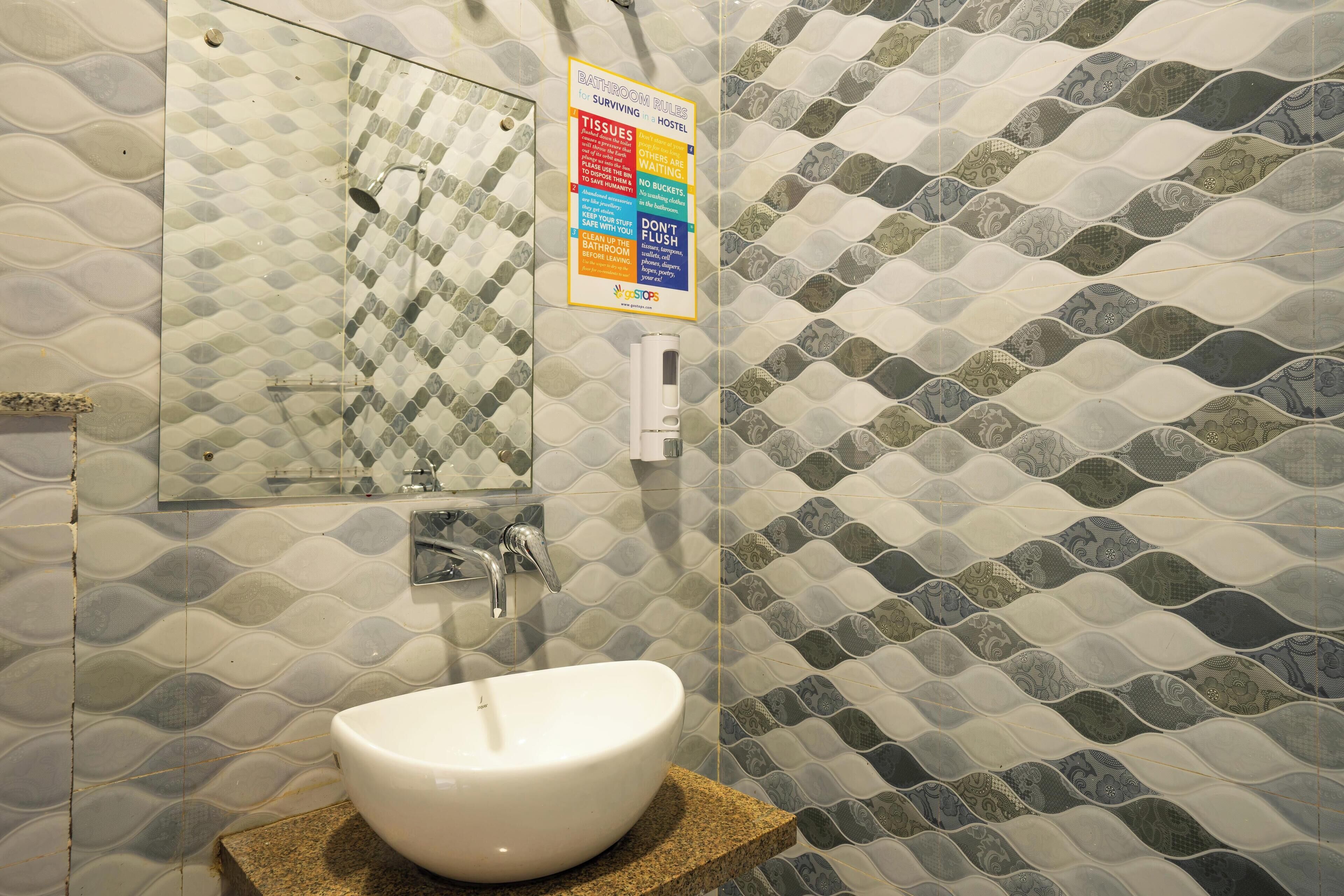 A bathroom with a white sink, a mirror, and a tiled wall with a wave pattern. There is a sign on the wall with text.