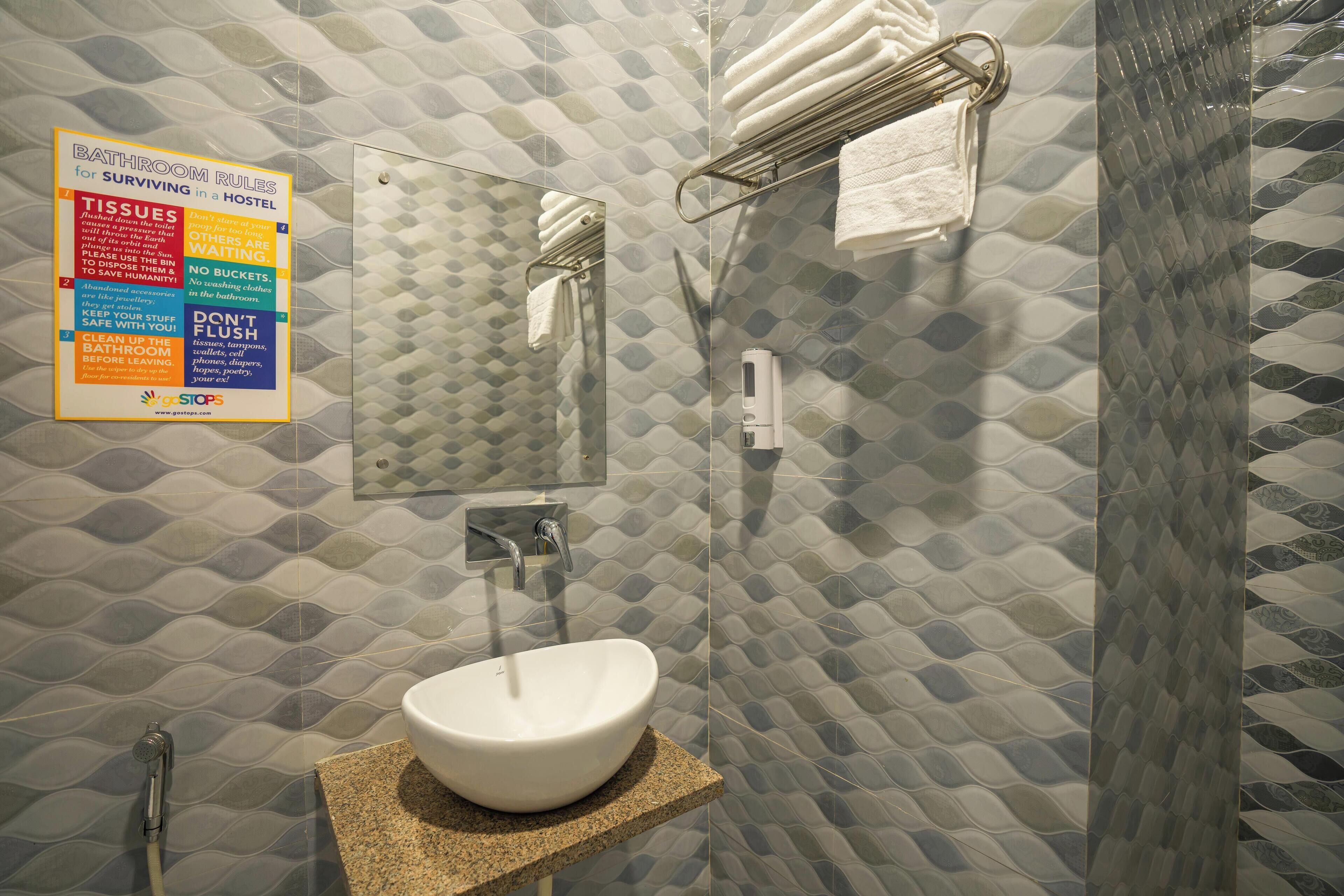 Une salle de bain avec un lavabo blanc, un porte-serviettes et une douche. Un panneau affiche les règles à respecter dans la salle de bain.