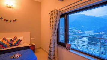 Una camera d'albergo con un letto, un comodino, una finestra vista città e montagne, e una tenda.