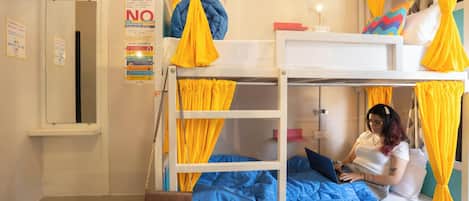 A bunk bed room with yellow curtains, a bed with a laptop, and a door with a sign.