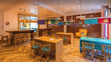 Café interno aberto 24 horas por dia, com mobiliário de madeira, luminárias pendentes e parede de tijolos.