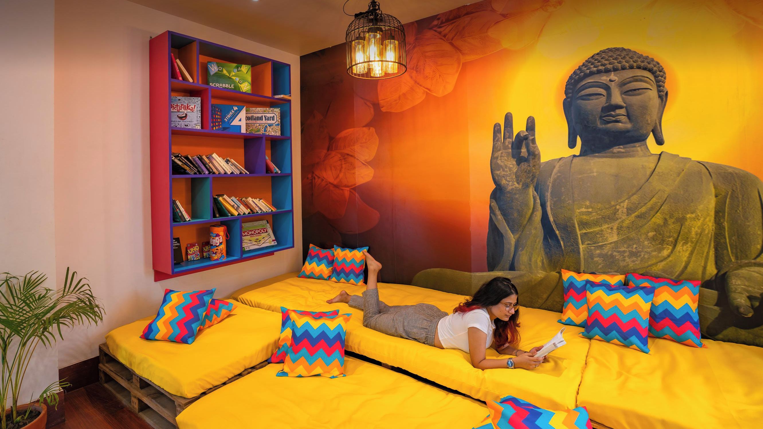 A room with a large Buddha statue, a bookshelf with colorful books, and a bed with zigzag patterned pillows.