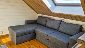 A loft bedroom with a sloped ceiling, a gray sectional sofa, wooden flooring, and a skylight. - 3 bedroom cozy apartment in Mandal (Mandal)