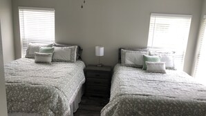 A bedroom with two beds, each with a floral-patterned bedspread, a bedside table with a lamp, and a window with blinds. - New Renovated House in Spanish Springs The Villages  (The Villages)