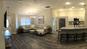 A modern kitchen with a central island, a dining area with a bar stool, and a living room with a sofa and a coffee table. - New Renovated House in Spanish Springs The Villages  (The Villages)