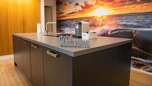 Une cuisine moderne agrémentée d’une pancarte « Bienvenue », d’une machine à café et d’une fresque murale représentant un magnifique coucher de soleil.
