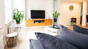 Un salon moderne doté d’un téléviseur à écran plat, de meubles en bois et de deux plantes en pot.