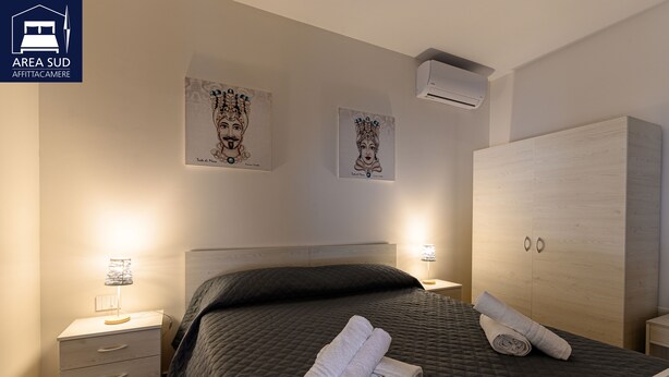 A hotel room with a bed, a wardrobe, a nightstand, and wall art. - South Area Guesthouse (self check-in) (Canicattì)