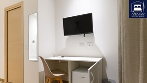 A compact room with a white desk, a chair, a small refrigerator, a television mounted on the wall, and a door. - South Area Guesthouse (self check-in) (Canicattì)
