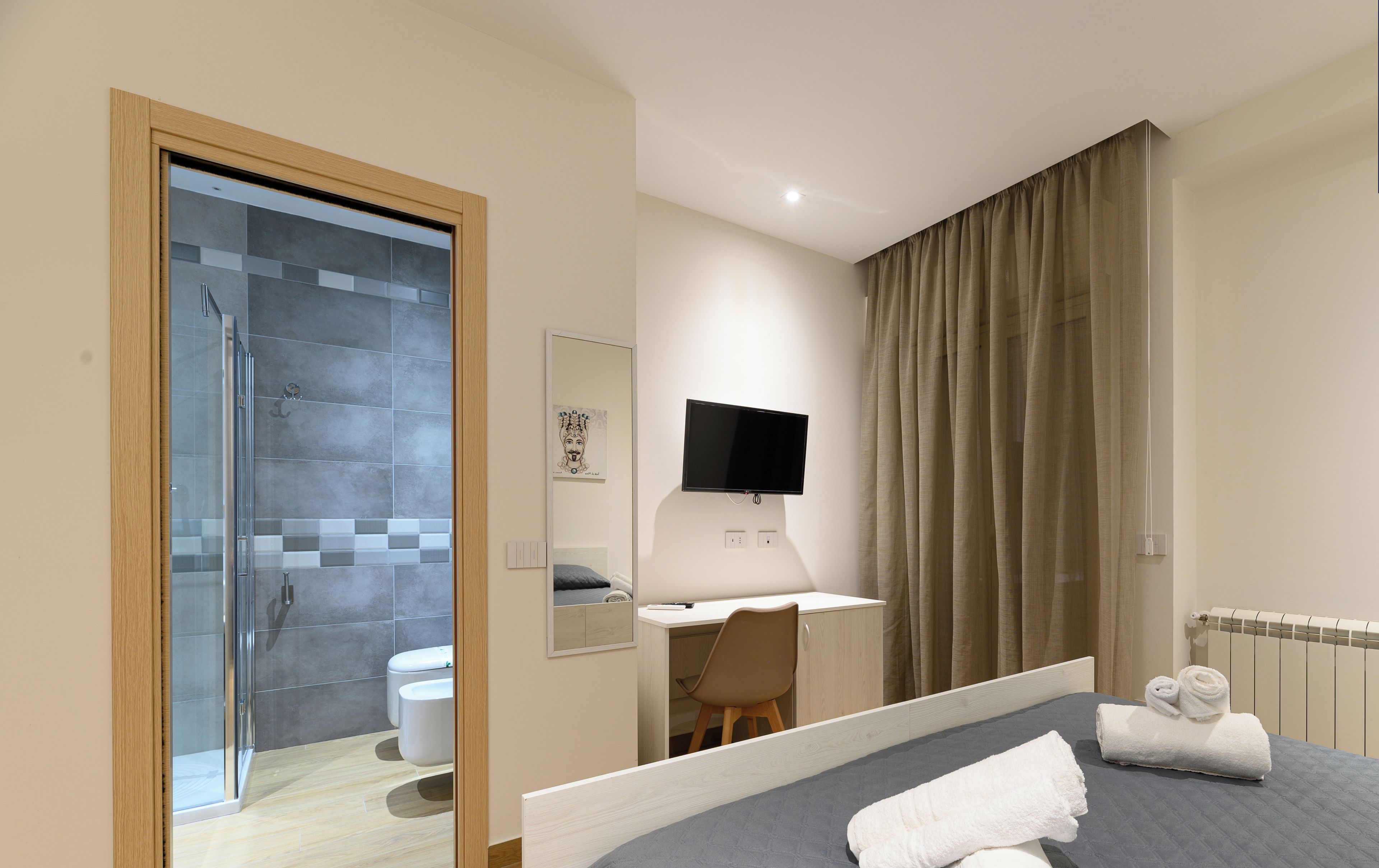 Ein modernes Hotelzimmer mit Bett, Schreibtisch, Dusche und Fernseher.