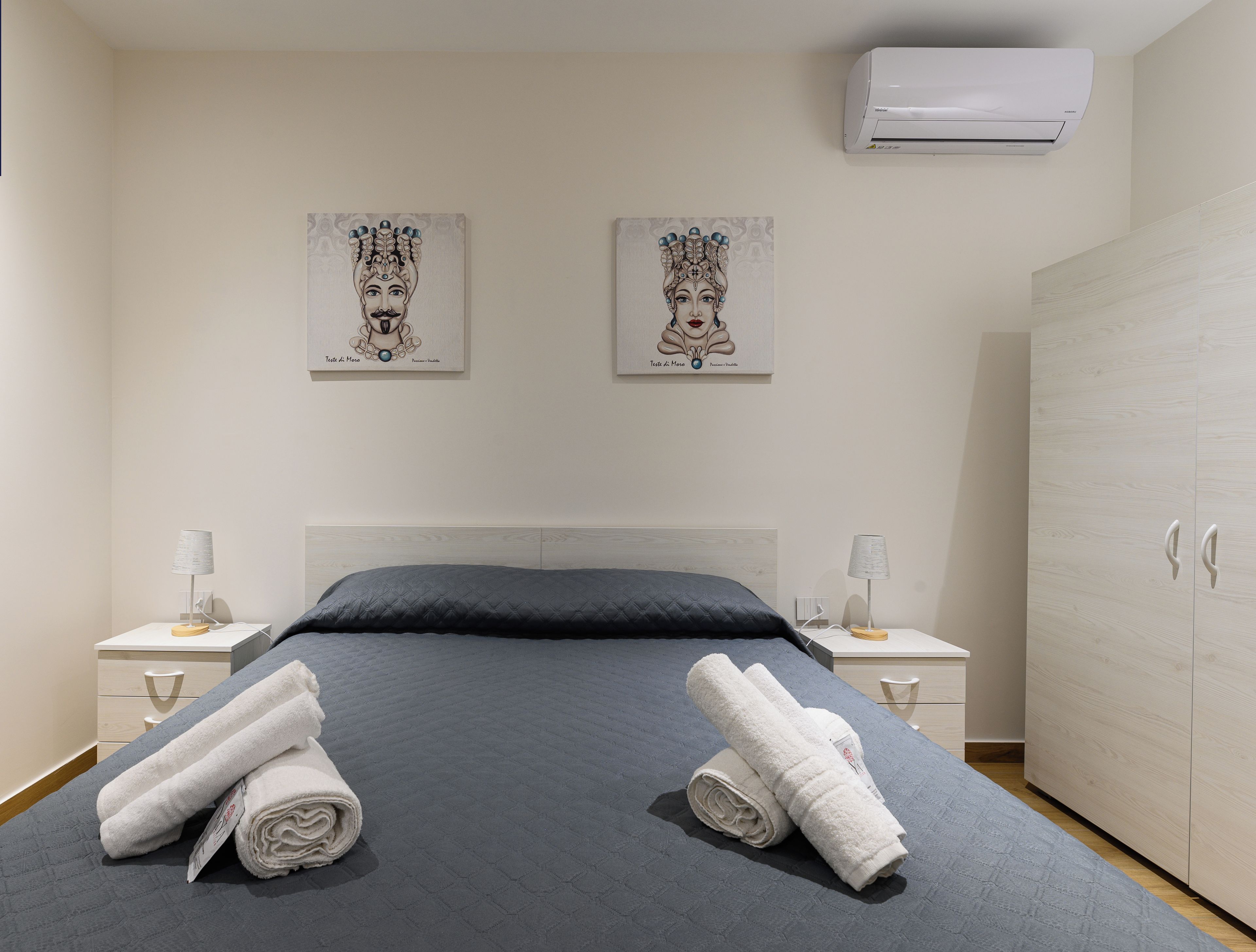 Une chambre d’hôtel comprenant un lit, deux tables de chevet, une armoire et deux climatiseurs fixés au mur.