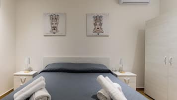 Une chambre d’hôtel comprenant un lit, deux tables de chevet, une armoire et deux climatiseurs fixés au mur.