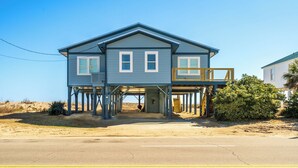A two-story house with a balcony and a covered entryway, elevated on stilts, located near a sandy beach. - 4 Bedroom 2 Bath Ocean Front Vacation Rental on Edisto Beach (Edisto Beach)