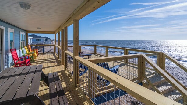 A wooden deck with a railing overlooking the beach, colorful Adirondack chairs, and a view of the ocean. - 4 Bedroom 2 Bath Ocean Front Vacation Rental on Edisto Beach (Edisto Beach)
