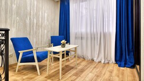 Une pièce avec un plancher en bois, deux chaises bleues, une petite table blanche et un vase rempli de fleurs.