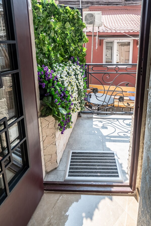 A doorway leading to a balcony with a stone wall, metal railing, and a view of a red building with a tiled roof.