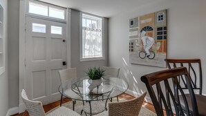 A dining area with a glass table surrounded by wicker chairs, a potted plant, and a wall-mounted artwork depicting a bicycle and a building with the word "KISTORANTE". - 4 Bedroom, 3  Bath  Big Downtown Frederick home, w/ Private Patio &  fire table (Frederick)