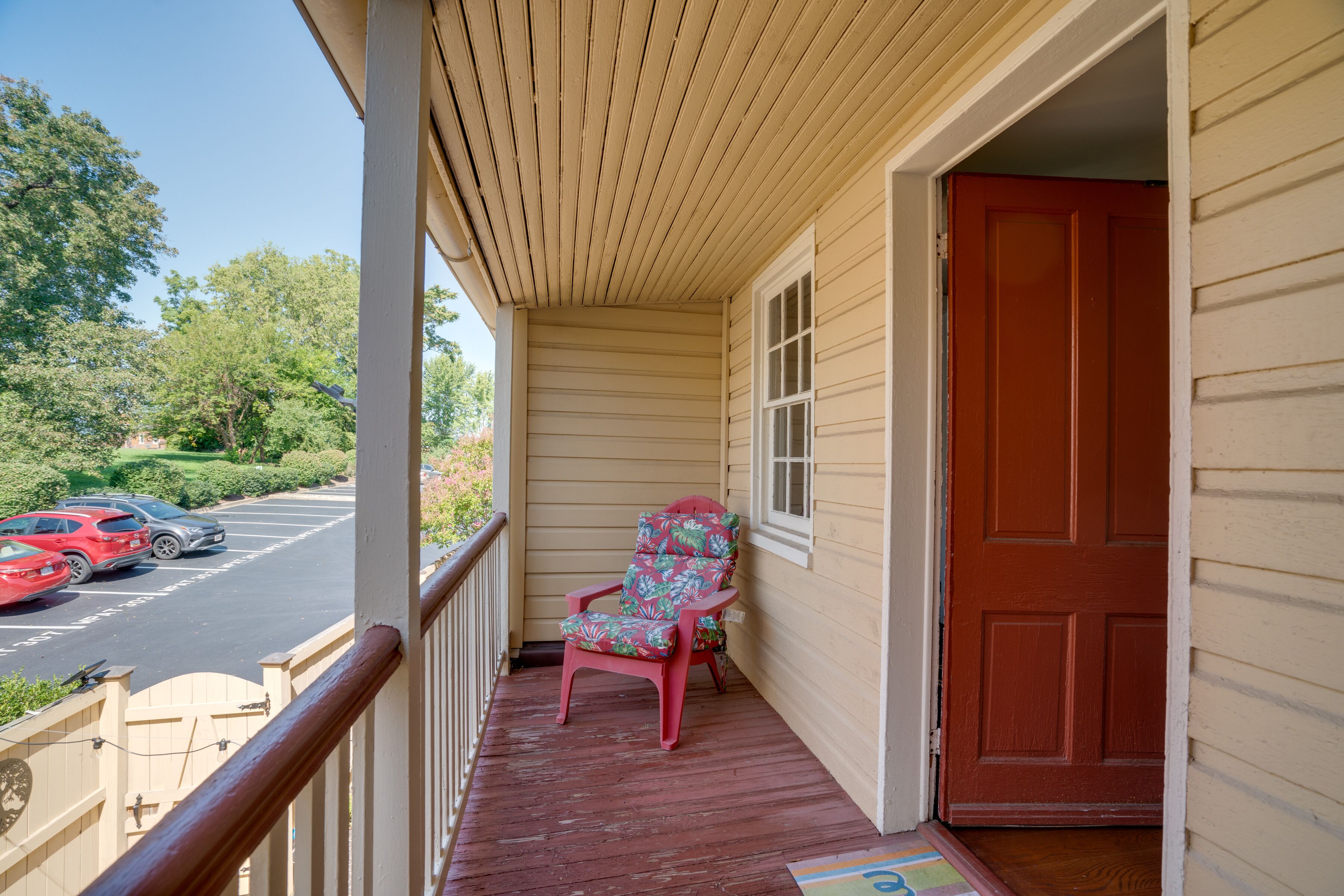 A porch with a wooden railing, a red door, and a patterned chair.