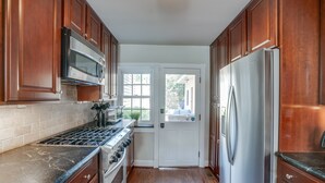 A kitchen with wooden cabinets, stainless steel appliances, and a white door leading outside. - 4 Bedroom, 3  Bath  Big Downtown Frederick home, w/ Private Patio &  fire table (Frederick)