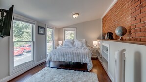 A bedroom with a bed, a white rug, a brick wall, and a window with a view of a red car. - 4 Bedroom, 3  Bath  Big Downtown Frederick home, w/ Private Patio &  fire table (Frederick)