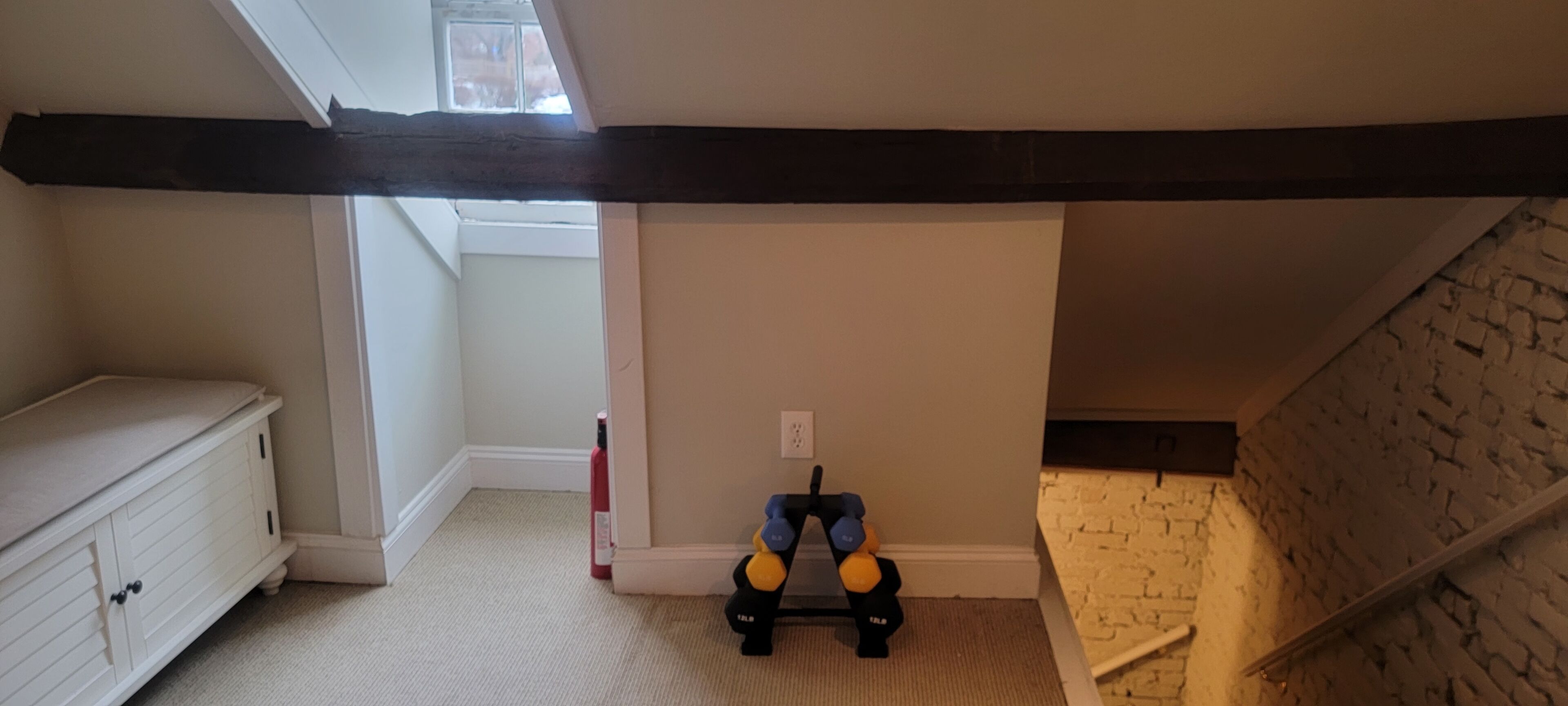 A room with a sloped ceiling, a white dresser, a toy with yellow and blue balls, and a brick wall.