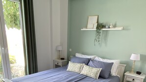 A bedroom with a bed, two bedside tables, a hanging light fixture, a wall-mounted shelf, and a window with curtains.