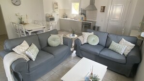 A modern living room with grey sofas, a white coffee table, and a kitchen in the background.
