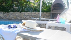A poolside area with lounge chairs, a hat, sunglasses, and a bottle on a table.