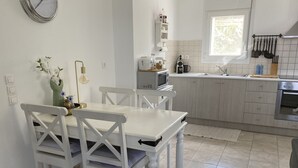 A kitchen with white cabinets, a dining table with chairs, a microwave, and a window.