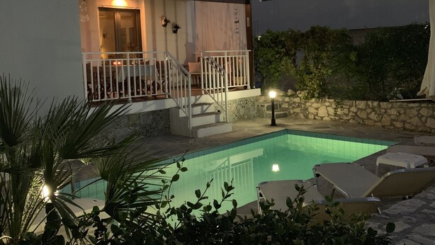 A modern villa with a swimming pool, outdoor seating, and a stone wall.