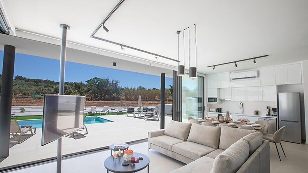 Un salon moderne doté d’une grande fenêtre, d’un canapé, d’une table basse et offrant une vue sur une piscine et un espace de détente extérieur.