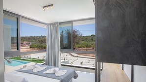 Une chambre d’hôtel moderne dotée d’un grand lit, offrant une vue sur une piscine et un paysage pittoresque.