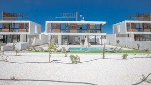 Un immeuble résidentiel moderne à plusieurs étages, doté d’une piscine, d’un espace extérieur aménagé et surplombant un ciel d’un bleu limpide.
