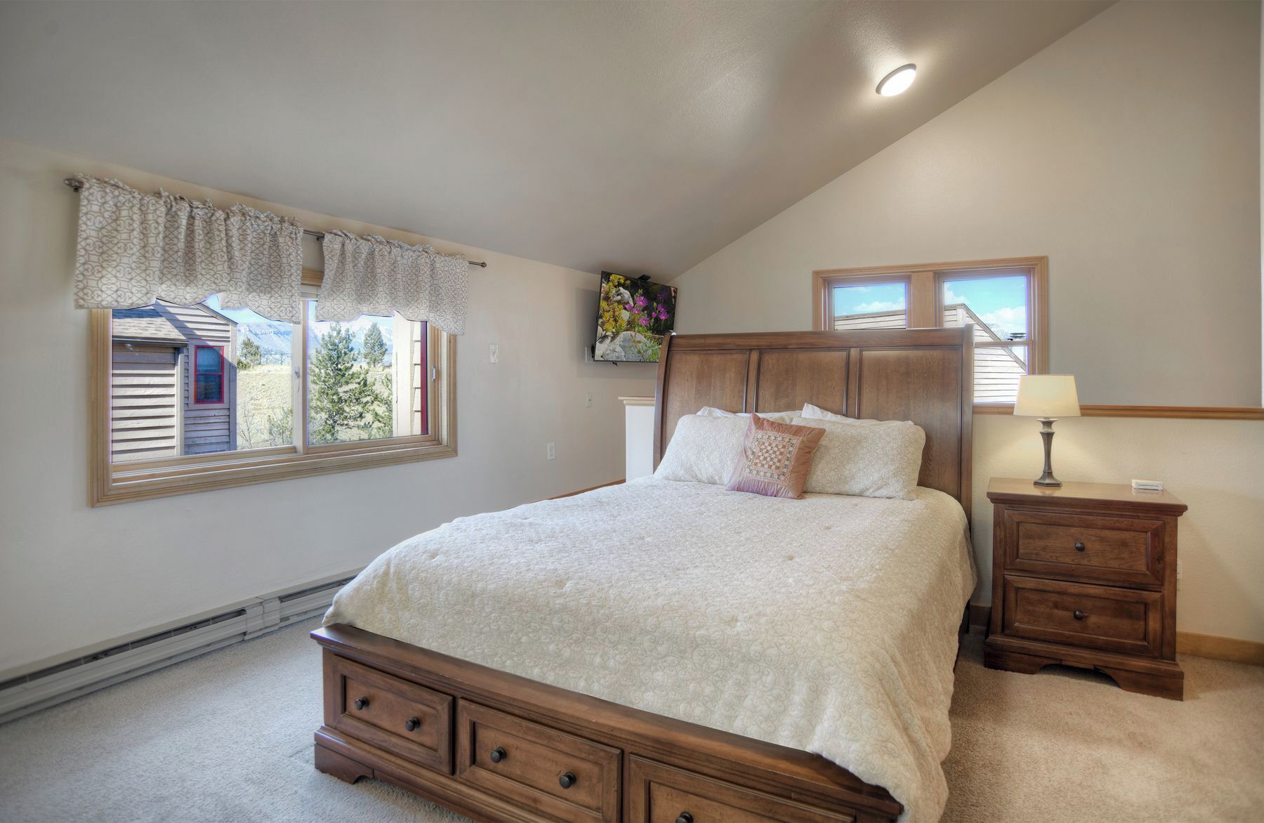 A bedroom with a large bed, a nightstand, a dresser, a window with curtains, and a ceiling light.