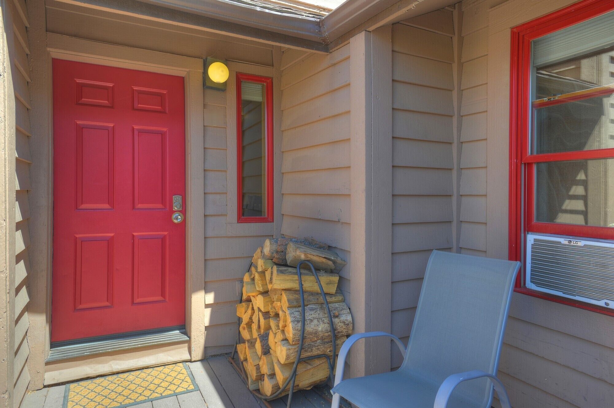 Une porte rouge avec une boîte aux lettres, une pile de bois de chauffage et une chaise devant une maison.
